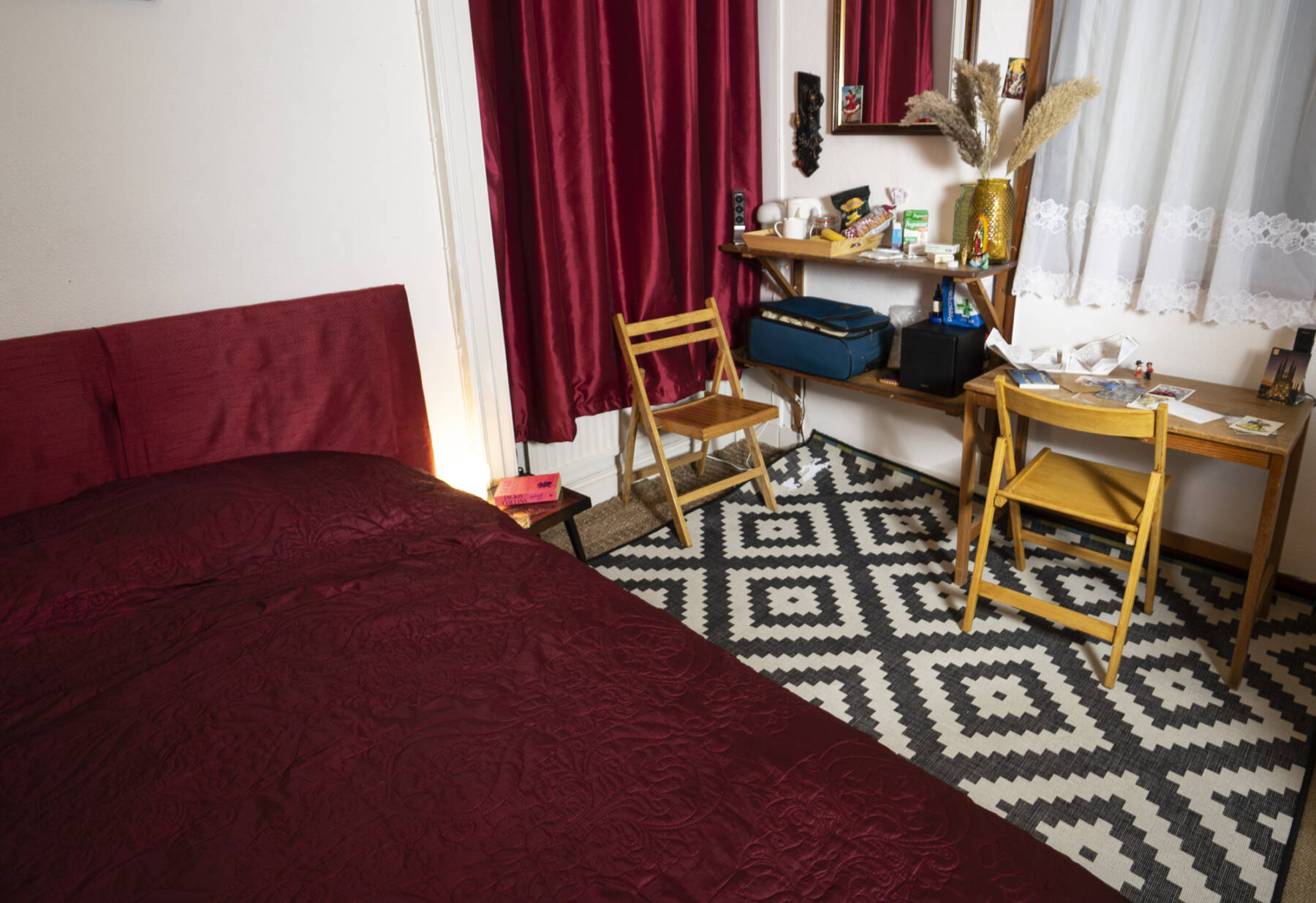 [gallery set up of a bedroom with cahirs and a desk, red duvet and red curtains and a black and white rug]