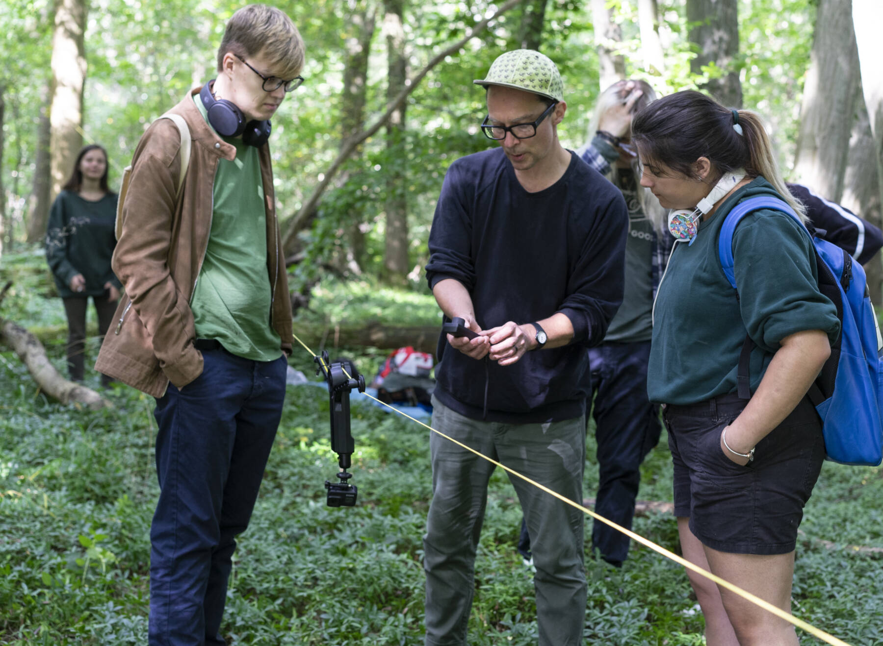 three people look at camera equipment in the woods on a workshop