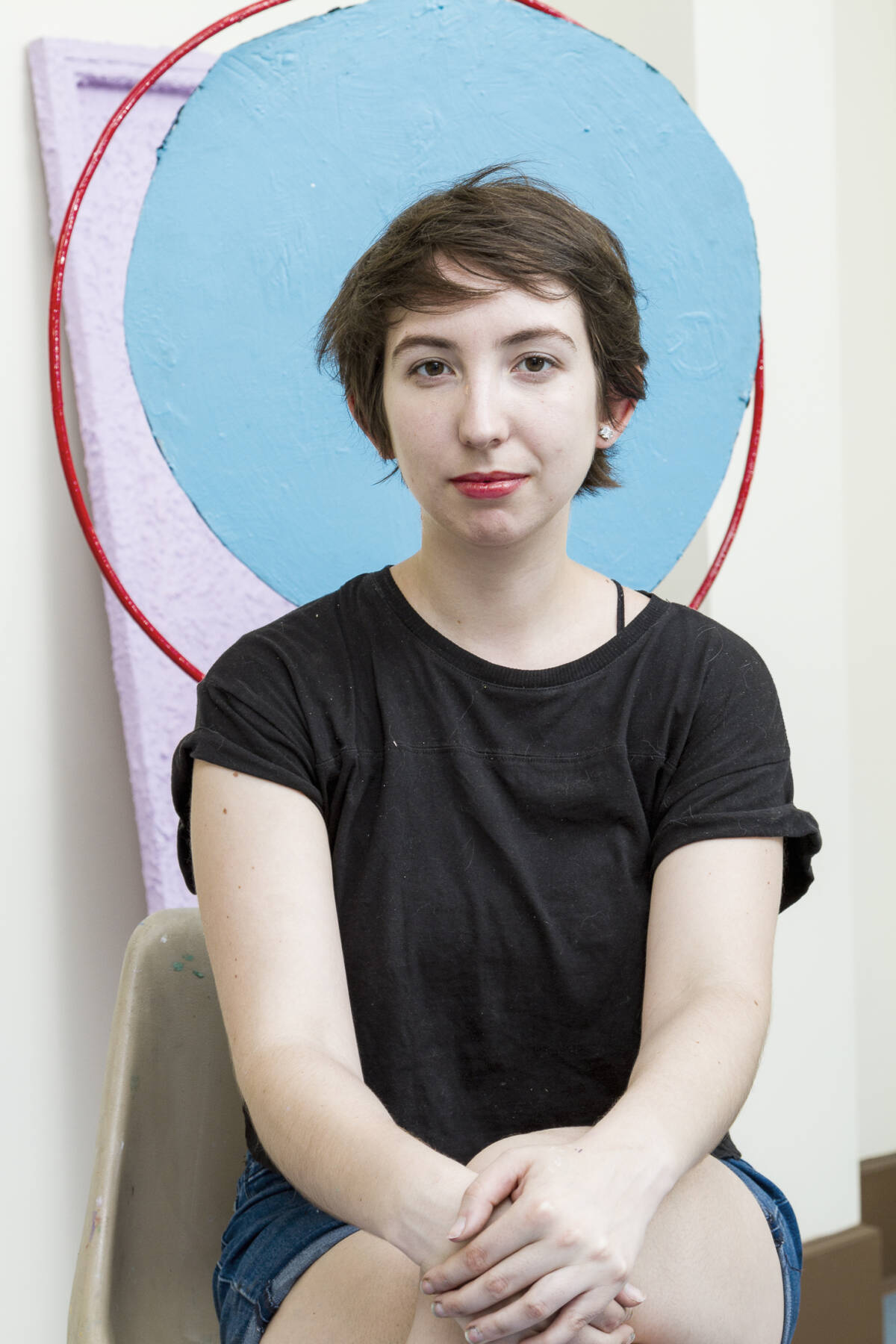 josefina-mellado wears a black t shirt with drak brown short hair and red lipstick infront of a baby blue graphic circl